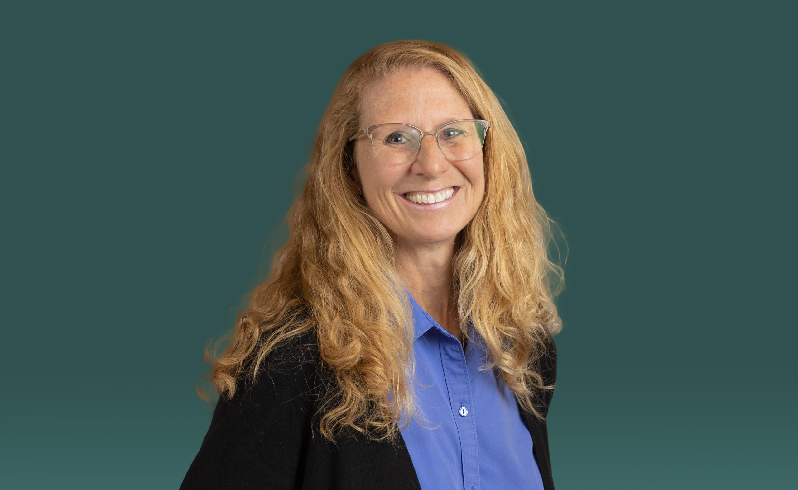 Event photography of a smiling woman with long hair and glasses against a green backdrop.