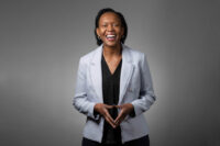 A smiling African woman in a corporate grey suit.