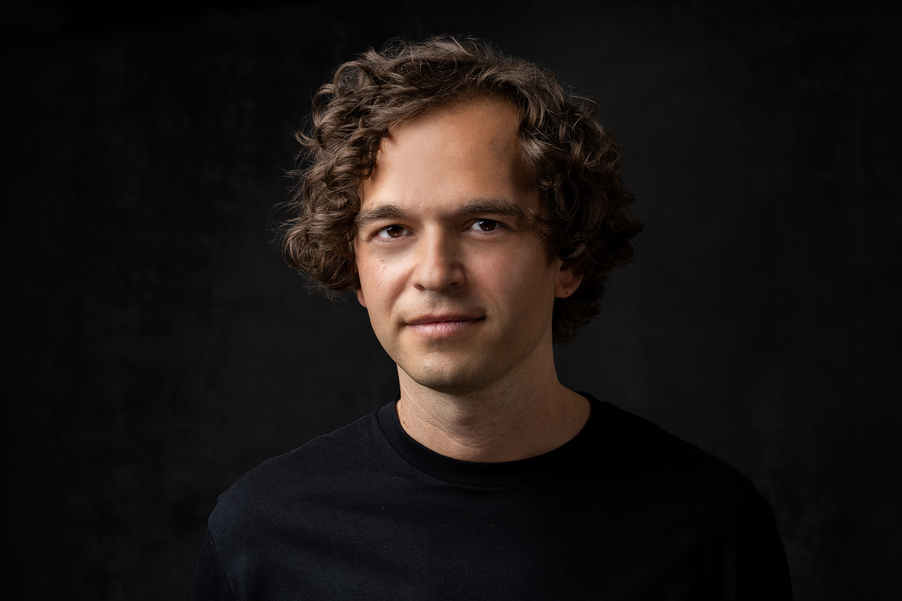 Portrait of a young man with curly hair against a dark background, captured in Denver headshots.