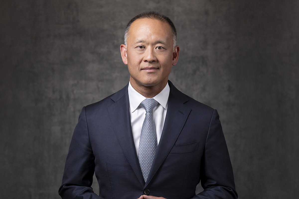 A man in a dark suit and tie stands against a gray background, looking directly at the camera with a neutral expression—perfectly capturing the professional quality one expects from Denver Headshot Co.