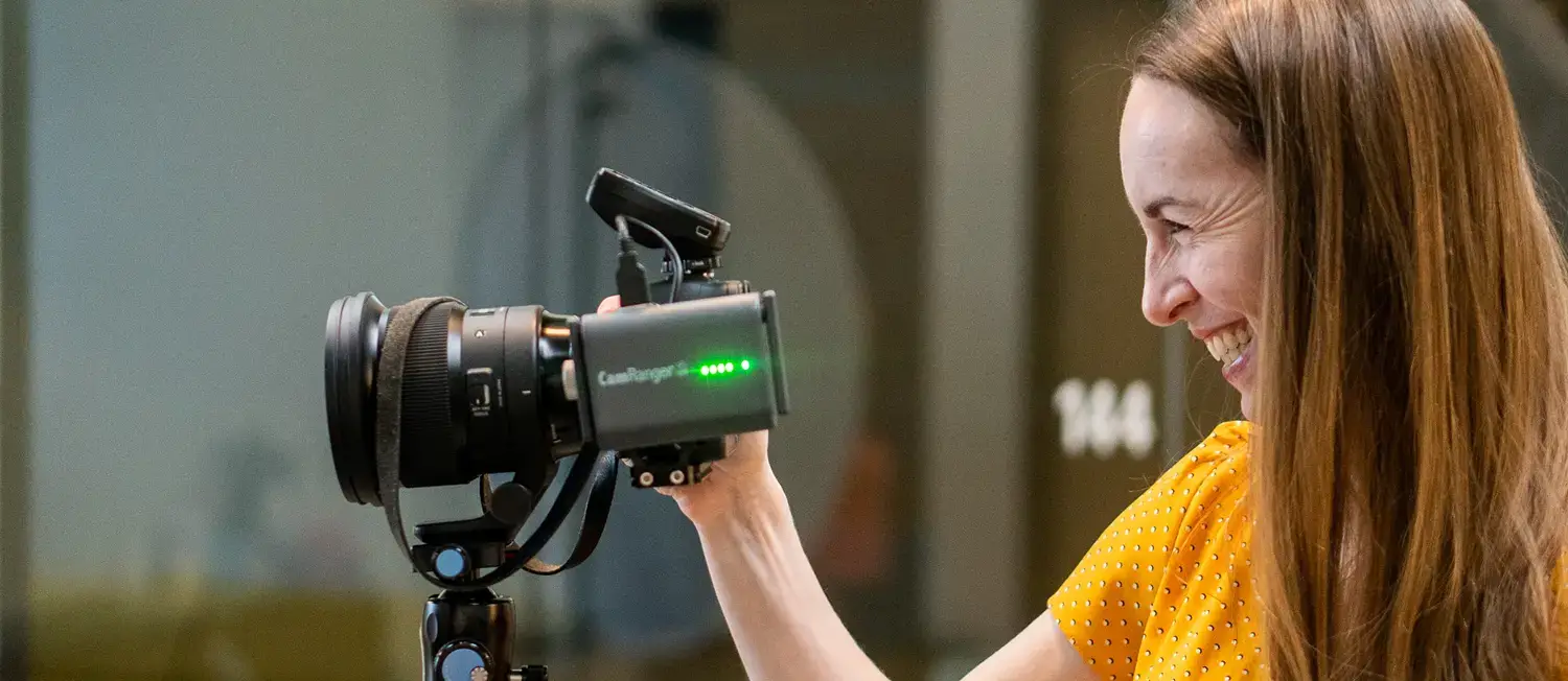 Person smiling while adjusting a professional camera on a tripod indoors.