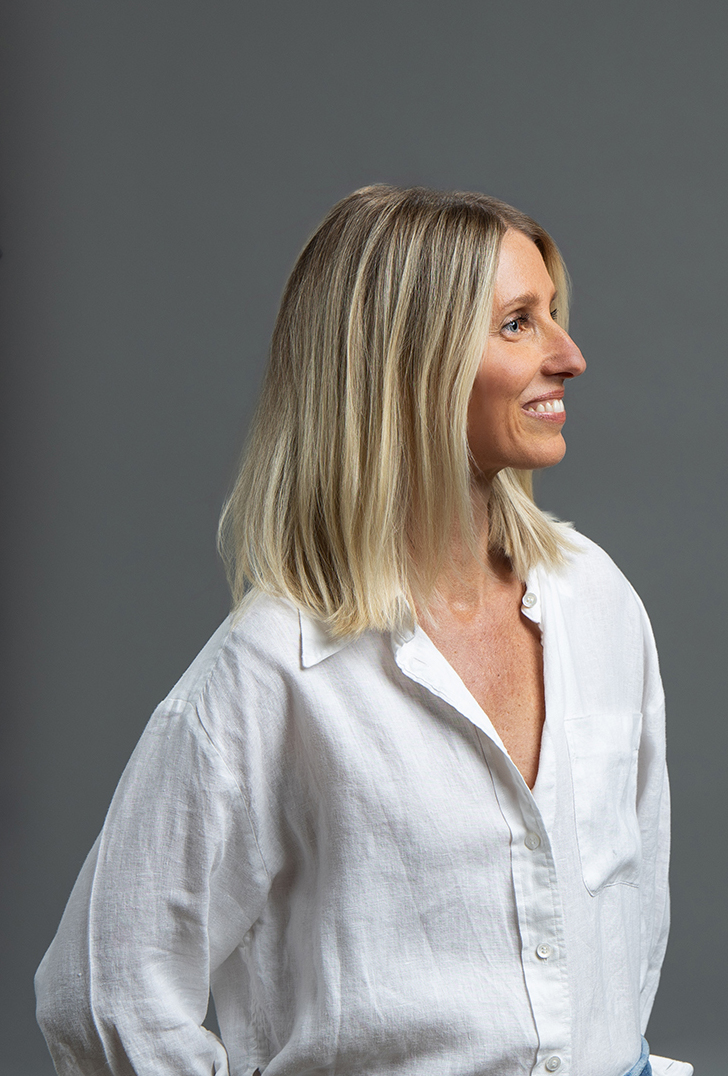 A woman with shoulder-length blond hair wearing a white shirt smiles while looking to the side, capturing the perfect moment for Denver Headshot Co.