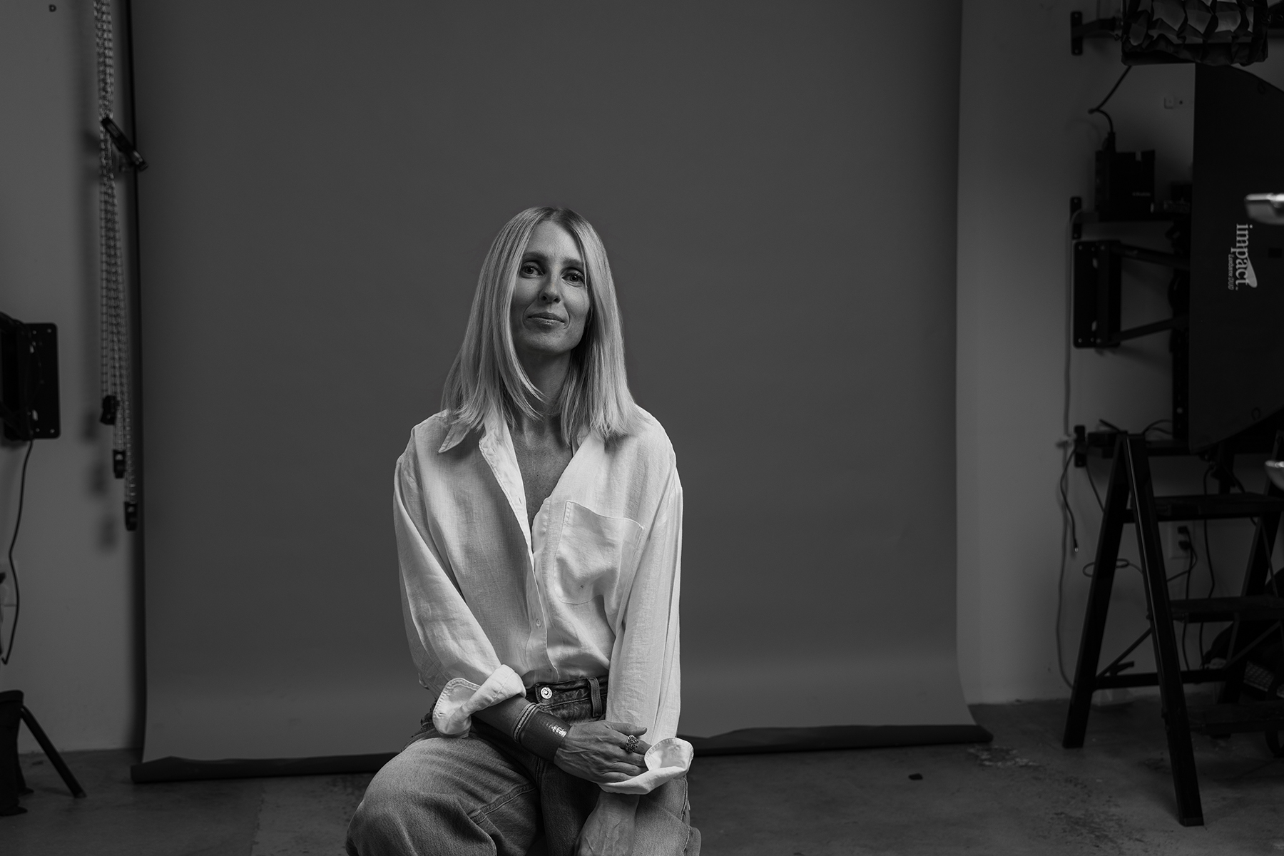 A person with shoulder-length hair sits in front of a backdrop, dressed in a light-colored shirt and pants. The setting, ideal for personal branding photography, appears to be a well-equipped studio.